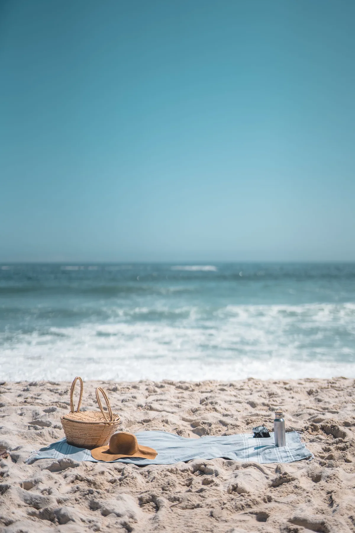 Tranquil beach scene with a picnic blanket, straw hat, and wicker basket by the sea