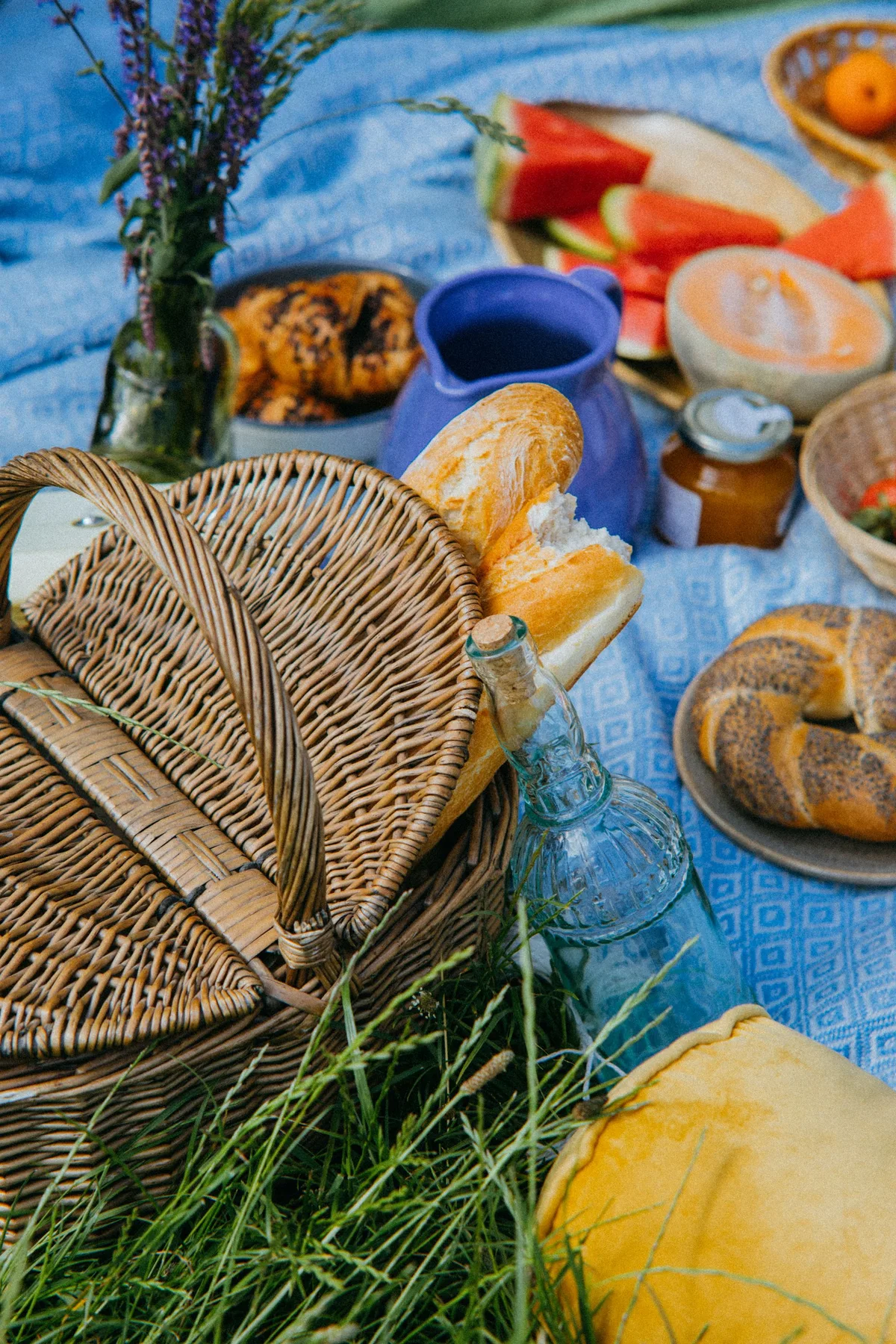 A vibrant outdoor picnic featuring breads, fruits, and a wicker basket on a blue blanket.